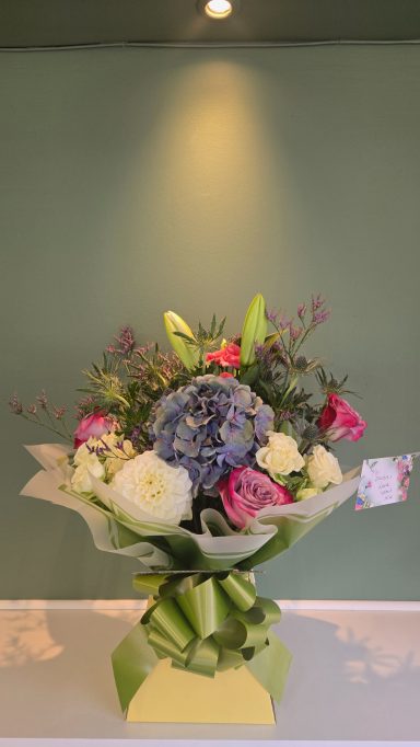 A bouquet of various flowers, including roses and hydrangeas, presented with greenery.