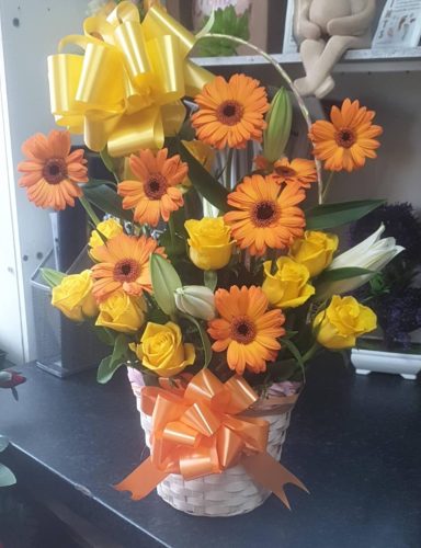 A basket of orange and yellow flowers with a yellow ribbon bow.