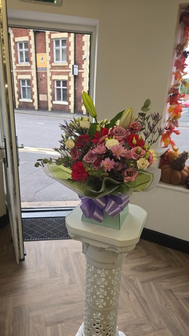 A vibrant flower bouquet in a vase, displayed on a pedestal near an open doorway.