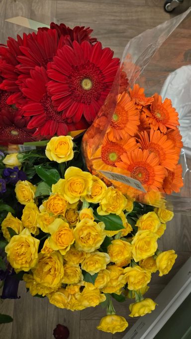 A vibrant bouquet with red gerberas, orange flowers, and yellow roses.