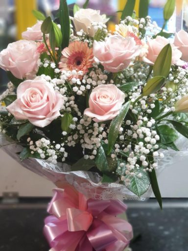 A bouquet of pink roses and gerbera daisies with baby's breath, wrapped with a pink ribbon.