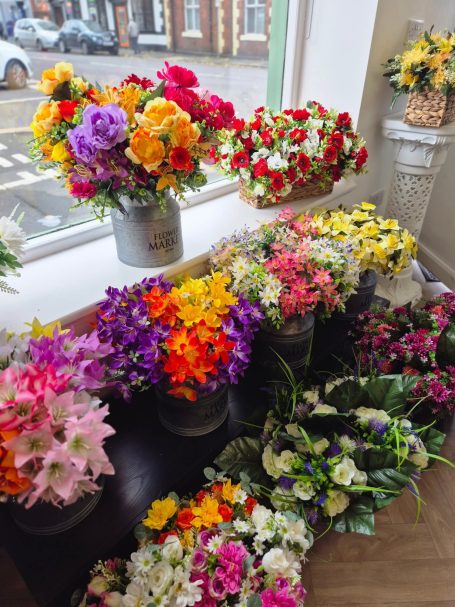 Vibrant bouquets of artificial flowers in various colours displayed in pots and containers.