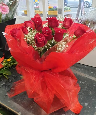 A bouquet of red roses wrapped in red tissue and white baby's breath.