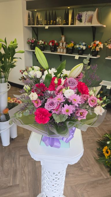 A vibrant bouquet of pink and white flowers with greenery on a display stand.