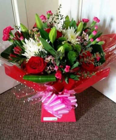 A vibrant bouquet featuring roses, lilies, and assorted greenery with pink wrapping.