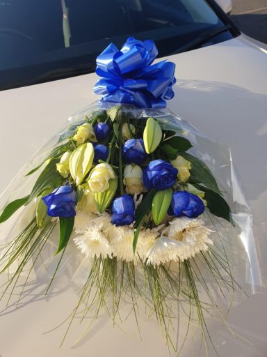 Bouquet of blue and white roses with greenery, wrapped in clear plastic.