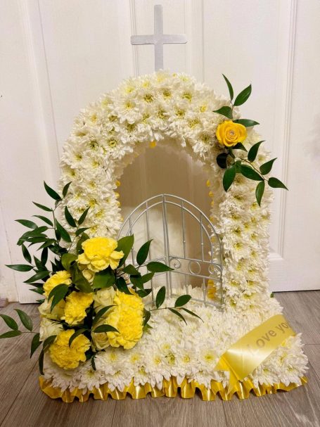 A decorative gates of heaven floral arrangement featuring white and yellow flowers with a cross motif.