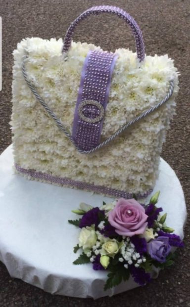 A cake designed as a handbag with floral decoration and a purple trim.