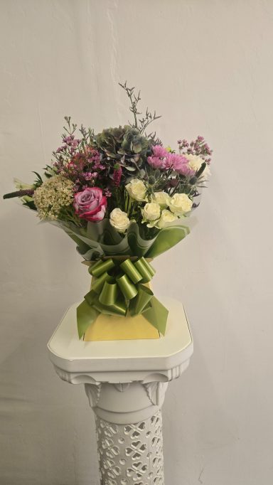 A bouquet of various flowers in soft colours, tied with a green ribbon.